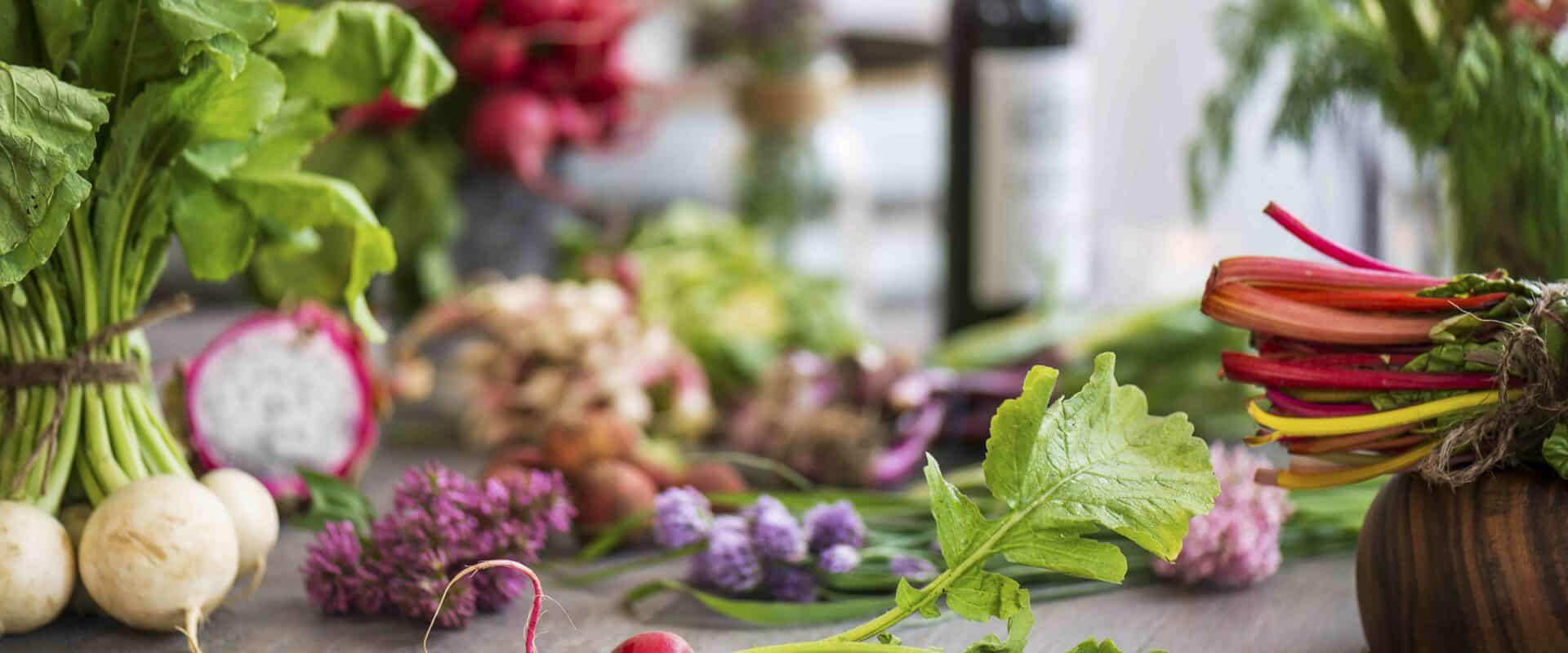 Single radish with lots of vegetables and flowers in the background